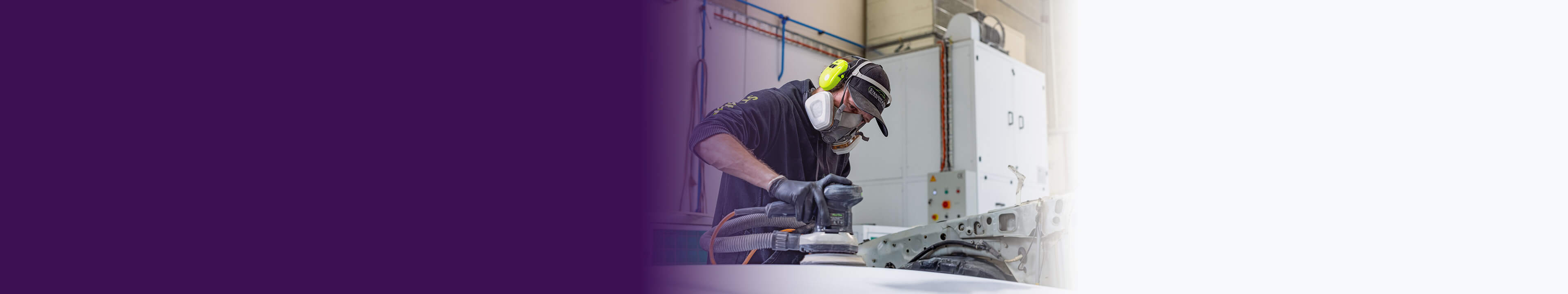 A man wearing protective gear, including a mask and gloves, can be seen diligently working on an automobile.