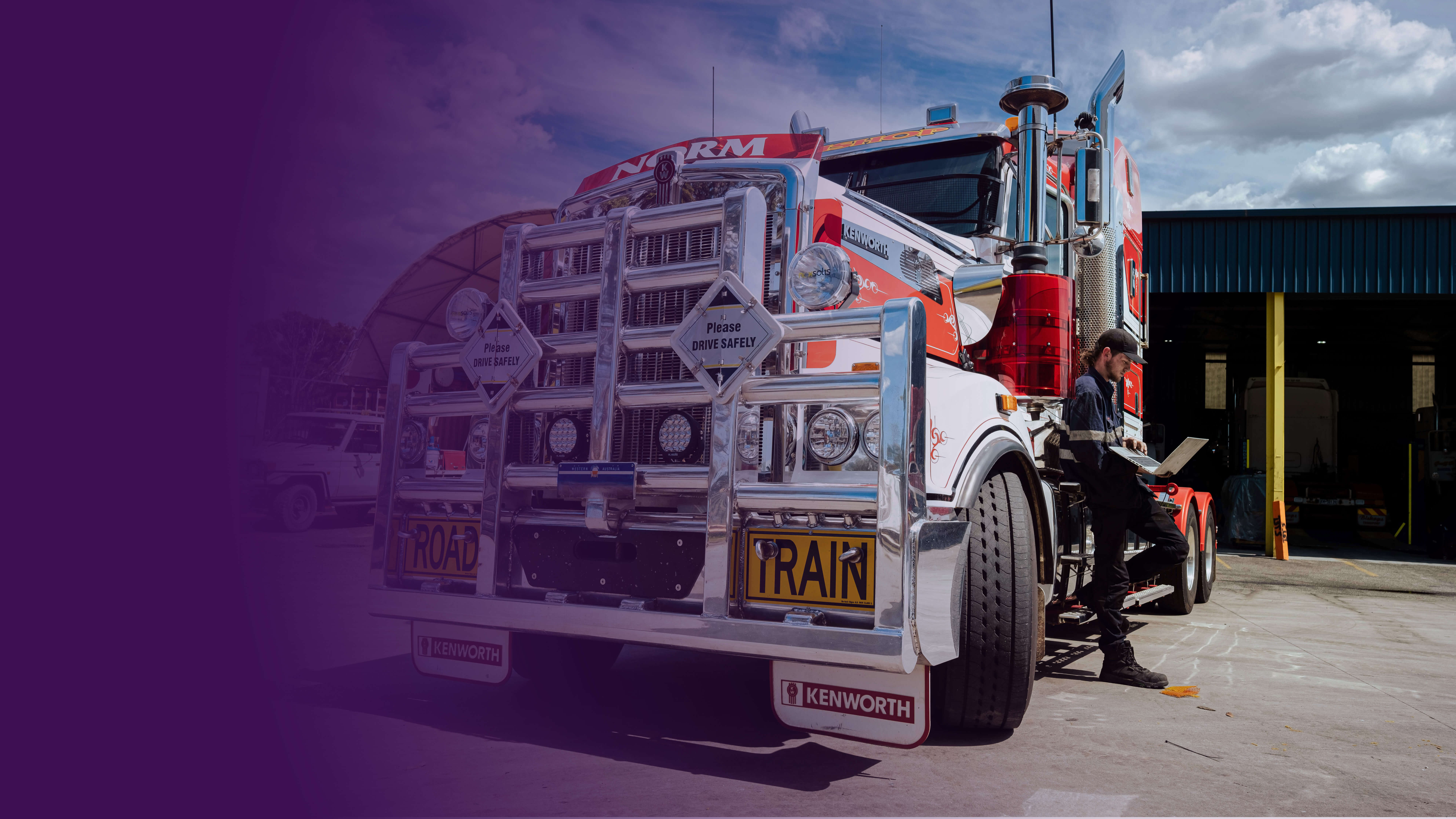 A mechanic stands beside a massive truck, attentively holding a computer, ready to diagnose and repair any potential issues.
