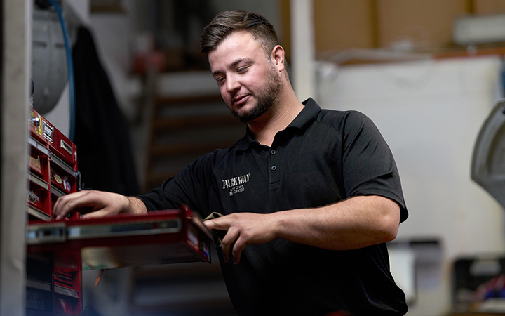 Donovan Le Roux reaching for tools in a workshop at Parkway Motors, standing beside a red tool chest in a professional garage.