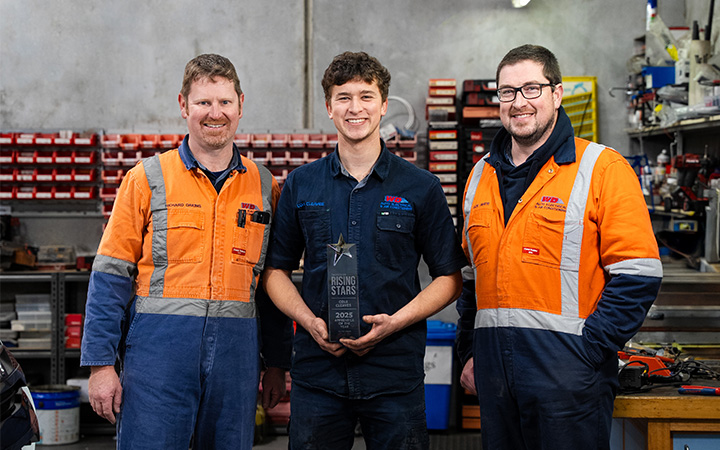 Three people in orange workwear stand in workshop, celebrating Cole Cleaves, 2025 Capricorn Rising Stars VIC/TAS Winner.