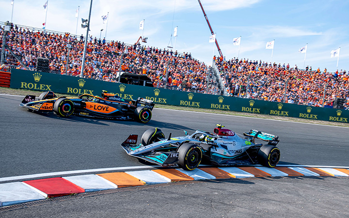 A thrilling scene of two F1 racing cars competing on the track, with a lively crowd cheering them on in the background.