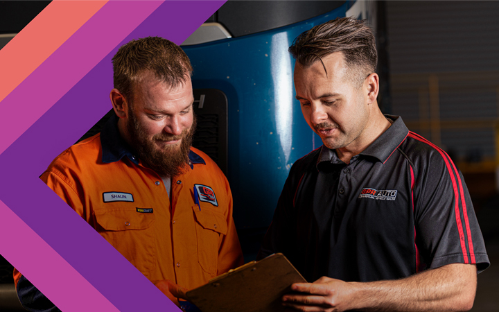 Two mechanics in a garage examining a sheet.