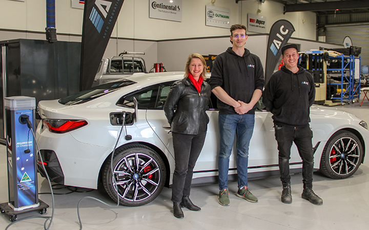 Vicky Ward - MP (left) with Jack Day (centre) and Stuart Chittenden (right) from Auto Innovation Centre (AIC) standing in front of an Eletcric Vehicle in their garage and smiling to the camera