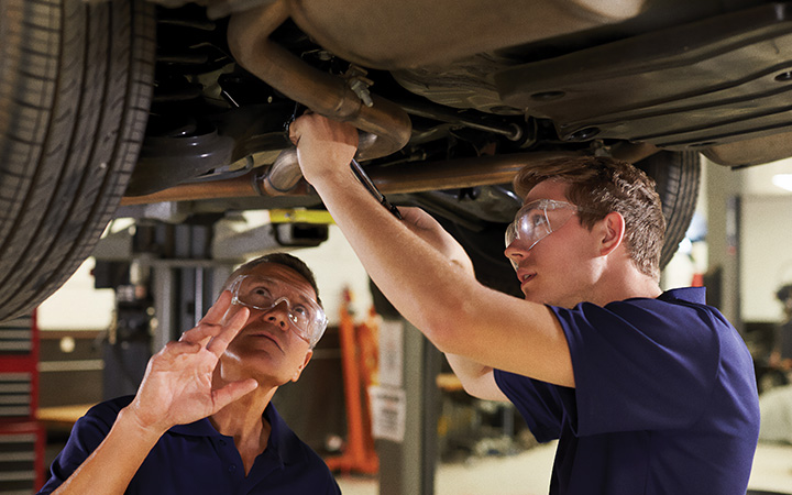 Apprentice working under a vehicle while being instructed by a technician