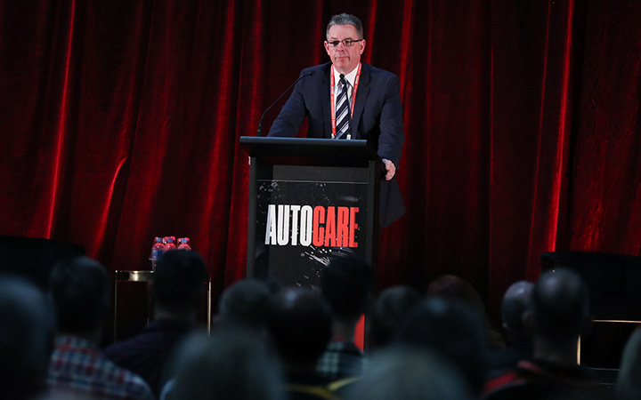 A person speaking on a stage at a previous Autocare event