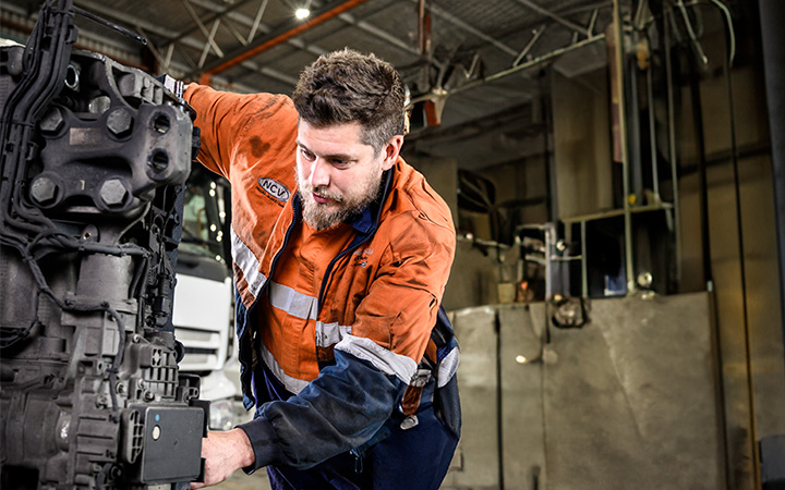 An auto technician working on a vehicle engine in a workshop.