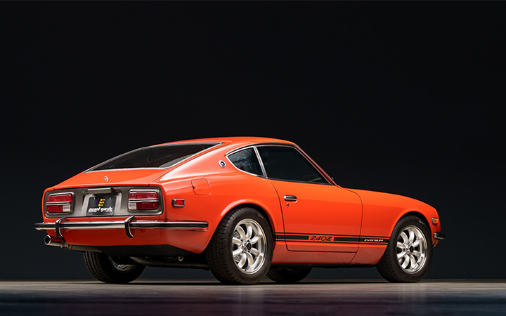 Datsun 240Z sports car with black stripes, showcased against a dark background.