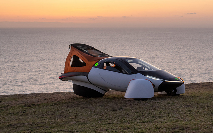 Sun-powered Aptera car parked on a green hill with a futuristic design.