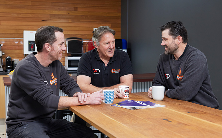 Three workshop team members enjoying a coffee break around a table, reflecting camaraderie and workplace culture