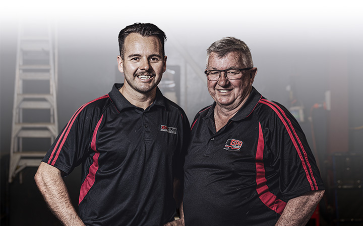 Two men in black and red shirts standing next to each other, smiling and posing for the camera.
