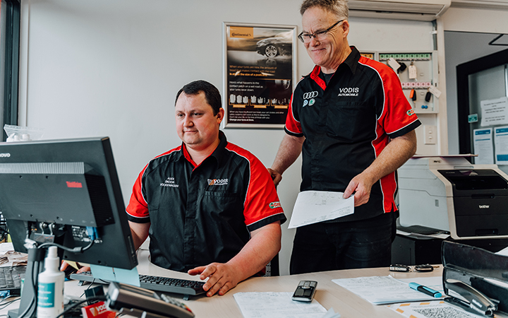 Two people in a business office focused on their computers, engaged in work tasks.