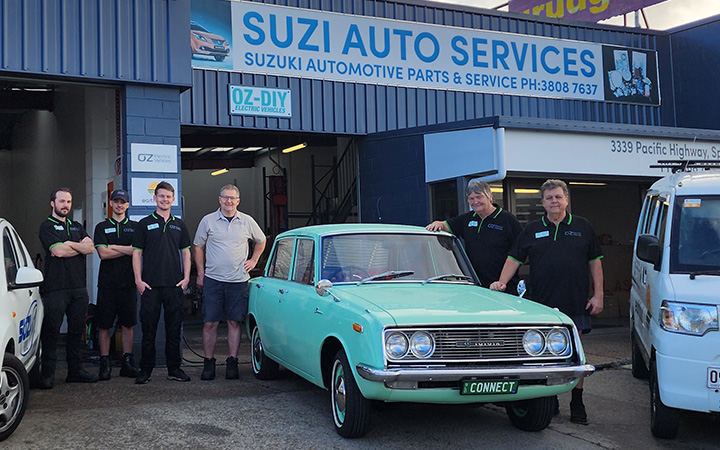 Six staff members of Oz EV in front of their workshop in the middle of some classic cars