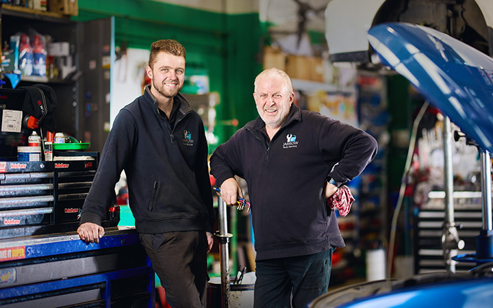 Stephen Rowe from Jarrow Auto Service and an employee, smile beside a blue car in a garage.