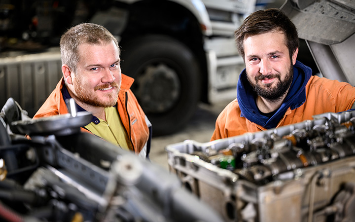 Two mechanics behind a truck's engineer smiling to the camera