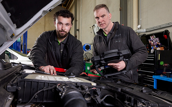 Two mechanics repairing a car engine in a workshop.