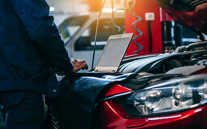 Mechanic working on a computer close to a car