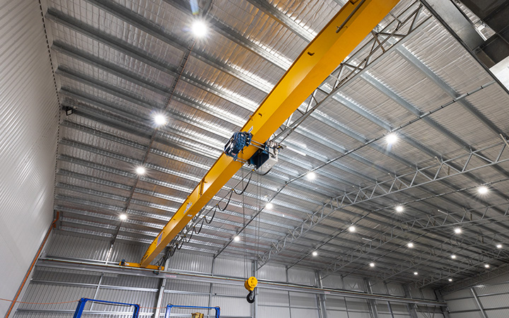 An expansive warehouse showcasing a crane and a metal door, brightly lit by LED lights