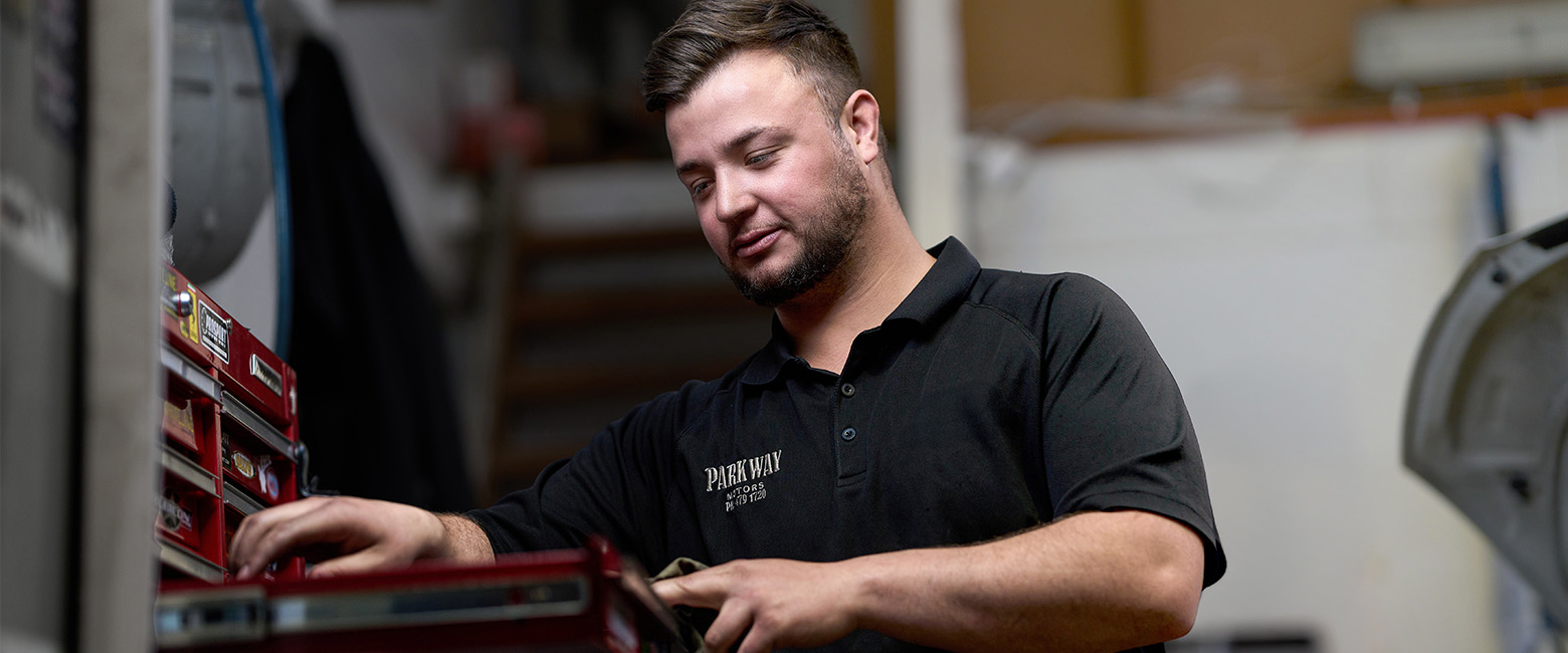 Donovan Le Roux reaching for tools in a workshop at Parkway Motors, standing beside a red tool chest in a professional garage.