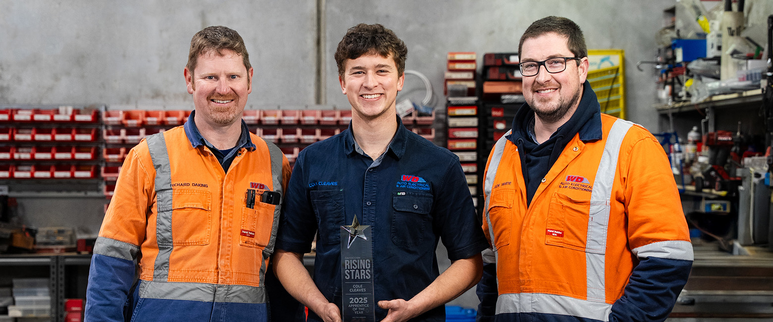 Three people in orange workwear stand in workshop, celebrating Cole Cleaves, 2025 Capricorn Rising Stars VIC/TAS Winner.