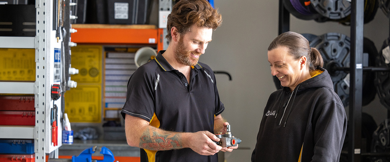 Two mechanics in a storage room, one of them holds a vehicle part.
