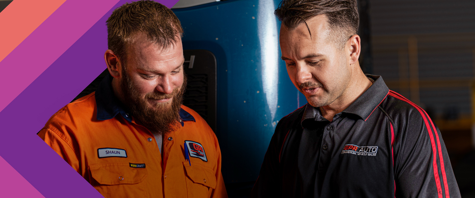 Two mechanics in a garage examining a sheet.