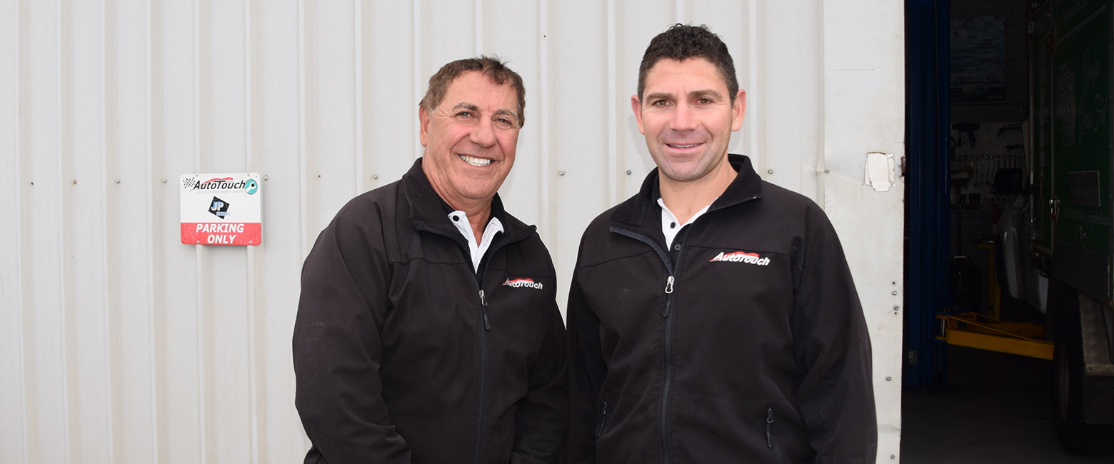 n front of the Autotouch workshop, Pino Priolo and his son Michael pose together, both smiling to the camera.
