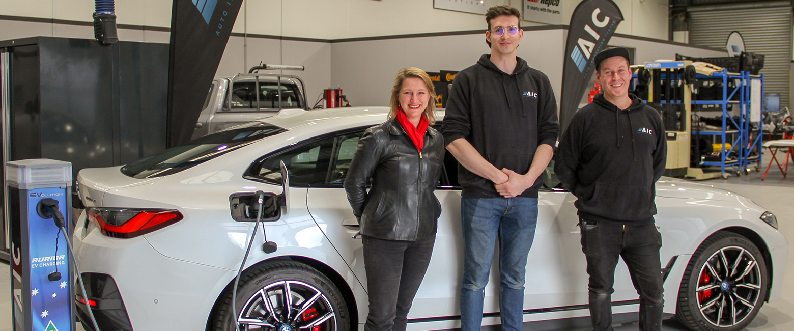 Vicky Ward - MP (left) with Jack Day (centre) and Stuart Chittenden (right) from Auto Innovation Centre (AIC) standing in front of an Eletcric Vehicle in their garage and smiling to the camera