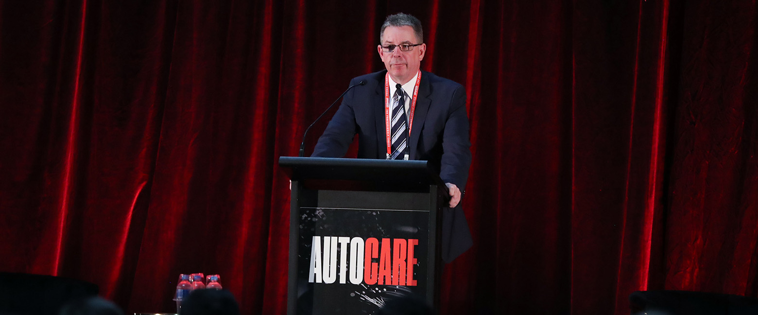 A person speaking on a stage at a previous Autocare event