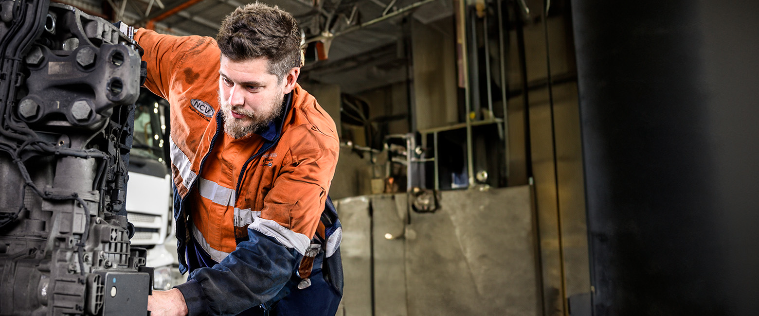 An auto technician working on a vehicle engine in a workshop.