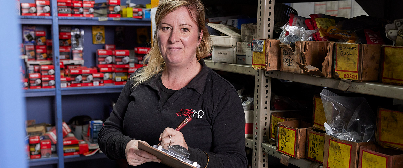 Woman taking notes and smiling to the camera in a workshop storage 