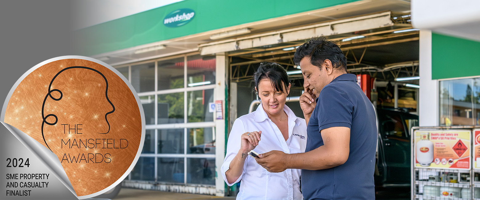 Capricorn Risk Account Manager talks with a Member in front of his workshop with a sticker overlay saying 'The Mansfield Awards 2024 SME Property and Casualty Finalist.