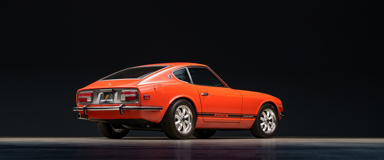 Datsun 240Z sports car with black stripes, showcased against a dark background.
