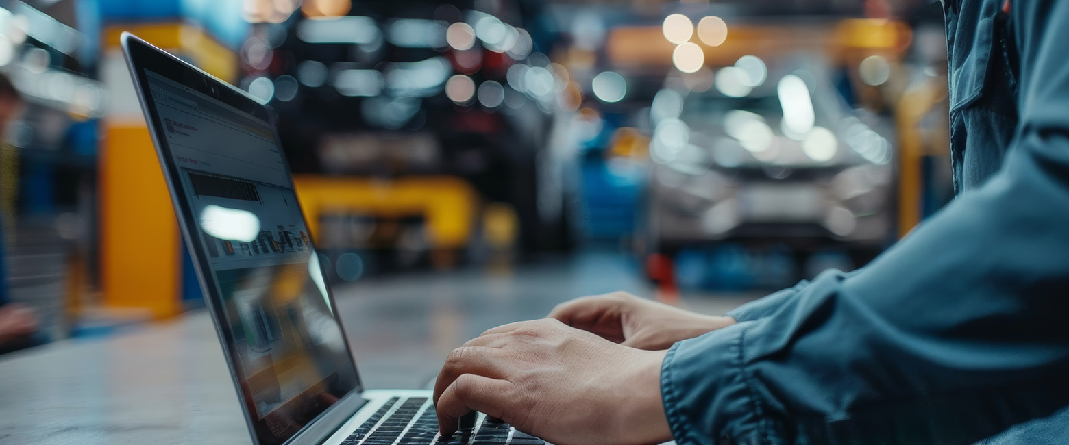 Person using a laptop in an automotive workshop, highlighting the importance of cyber security in modern vehicle services