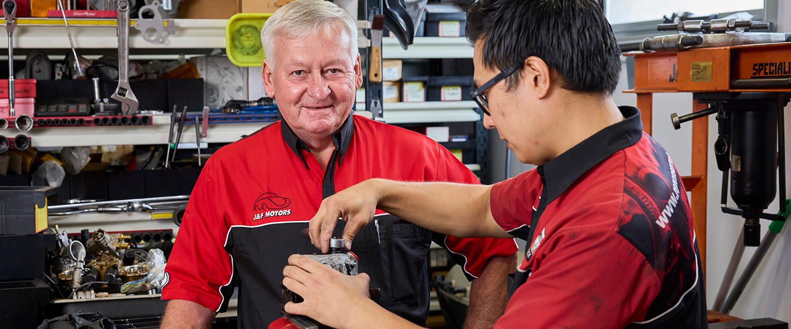 Two mechanics are actively working on a machine in a workshop, showcasing teamwork and technical skills.