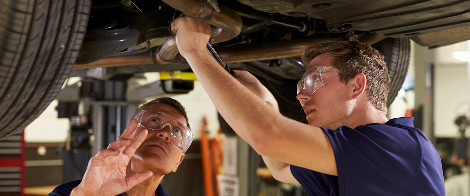 Two mechanics repairing a car underneath it, using tools and working together to fix the vehicle.