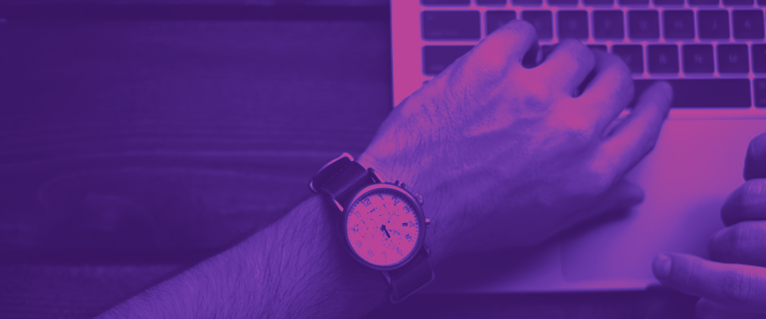 A hand typing on a computer and a watch on the wrist showing 5pm