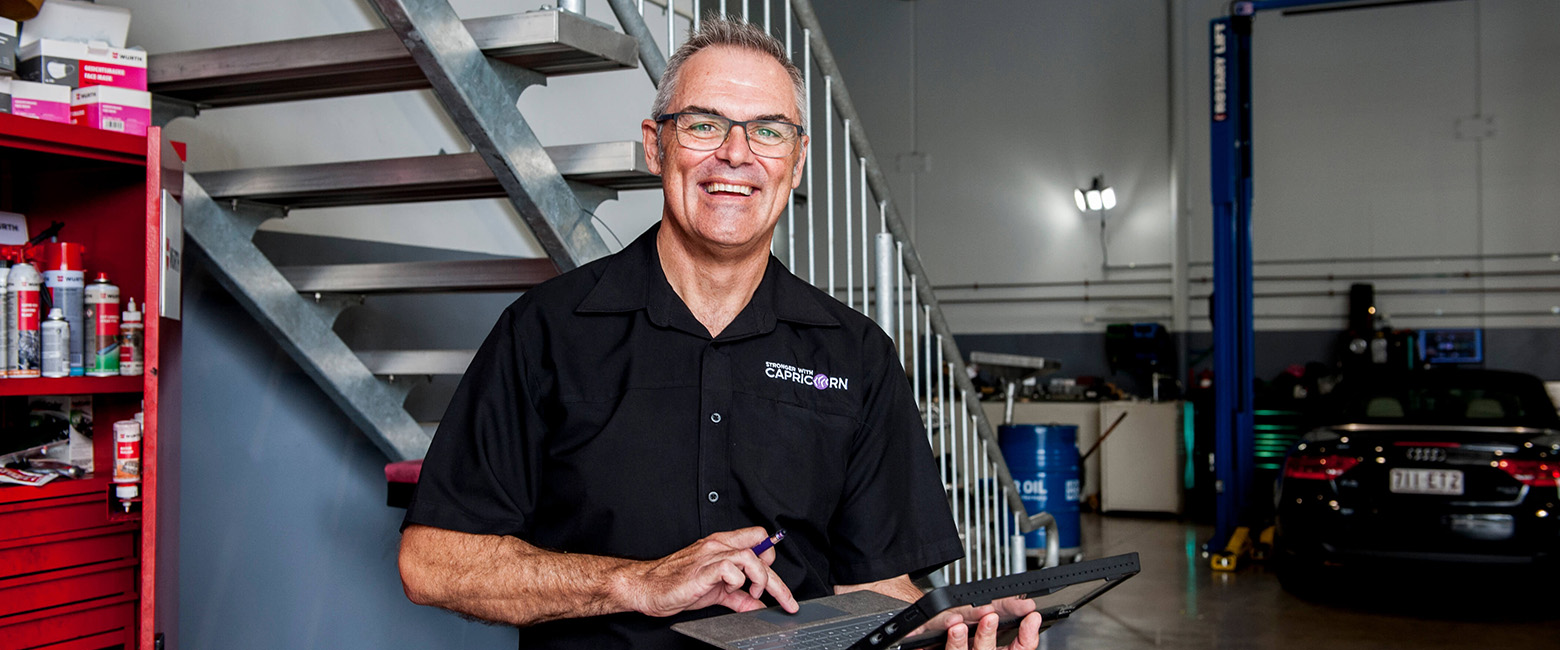 In a garage, a Capricorn Area Manager in a black shirt is engaged with a laptop.