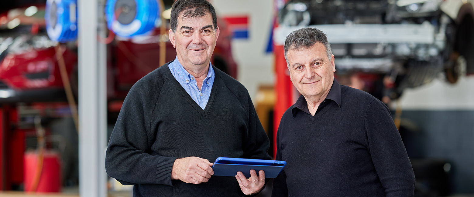 Two men, Larry and Frank Napoli, are seen in a car repair shop, holding a tablet.