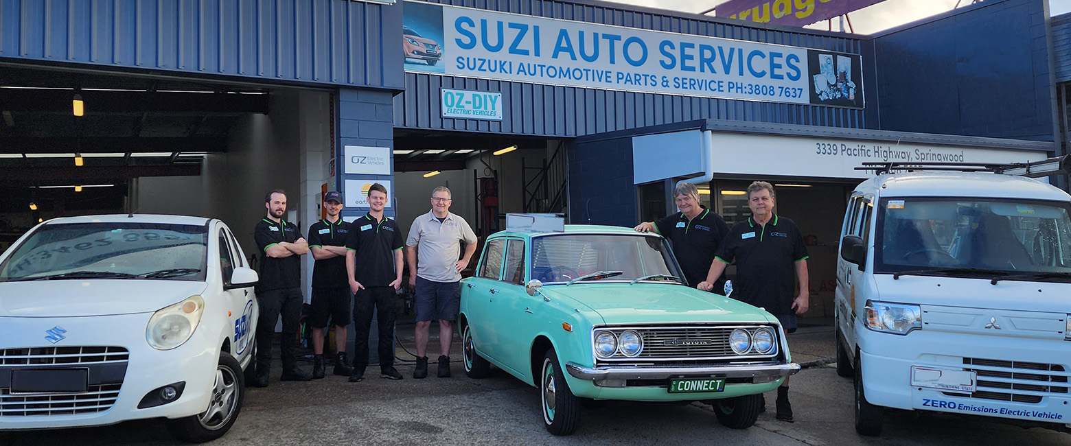 Six staff members of Oz EV in front of their workshop in the middle of some classic cars
