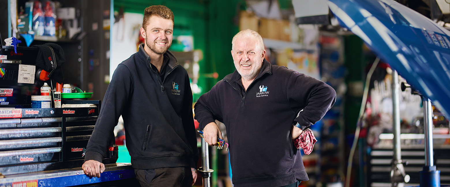 Stephen Rowe from Jarrow Auto Service and an employee, smile beside a blue car in a garage.