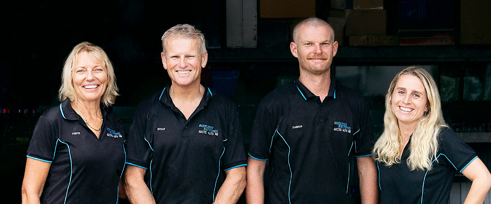 Four Capricorn Members standing together in front of Beenleigh Batteries workshop, wearing black polo shirts with blue accents. From left to right: Steve’s wife, Steve, Darren, and Mikayla, smiling to the camera.