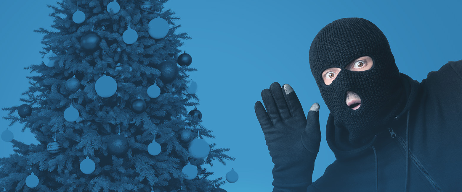 A person in a black mask and hoodie stands by a Christmas tree.