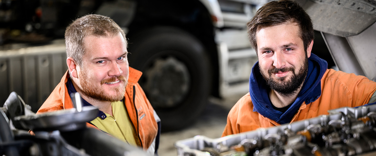 Two mechanics behind a truck's engineer smiling to the camera