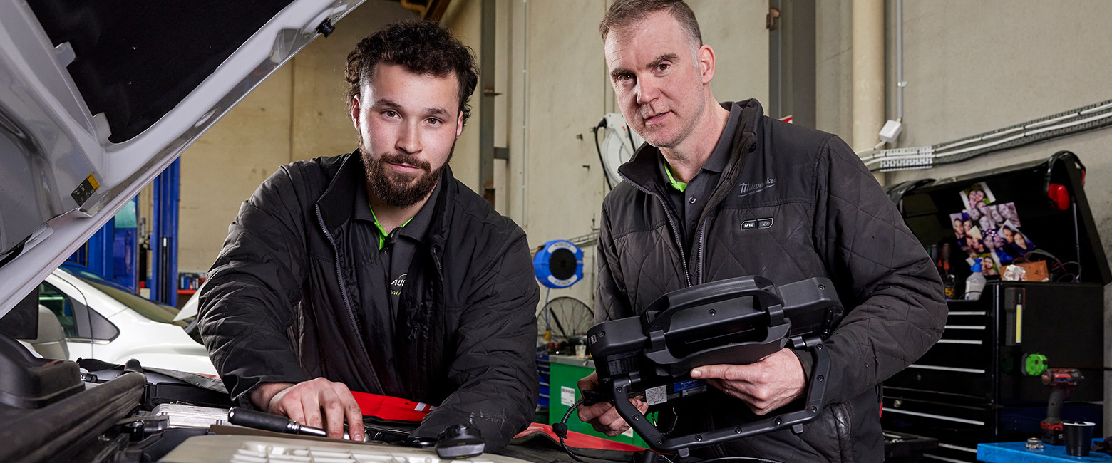 Two mechanics repairing a car engine in a workshop.