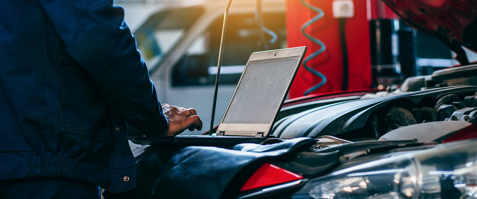 Mechanic working on a computer close to a car
