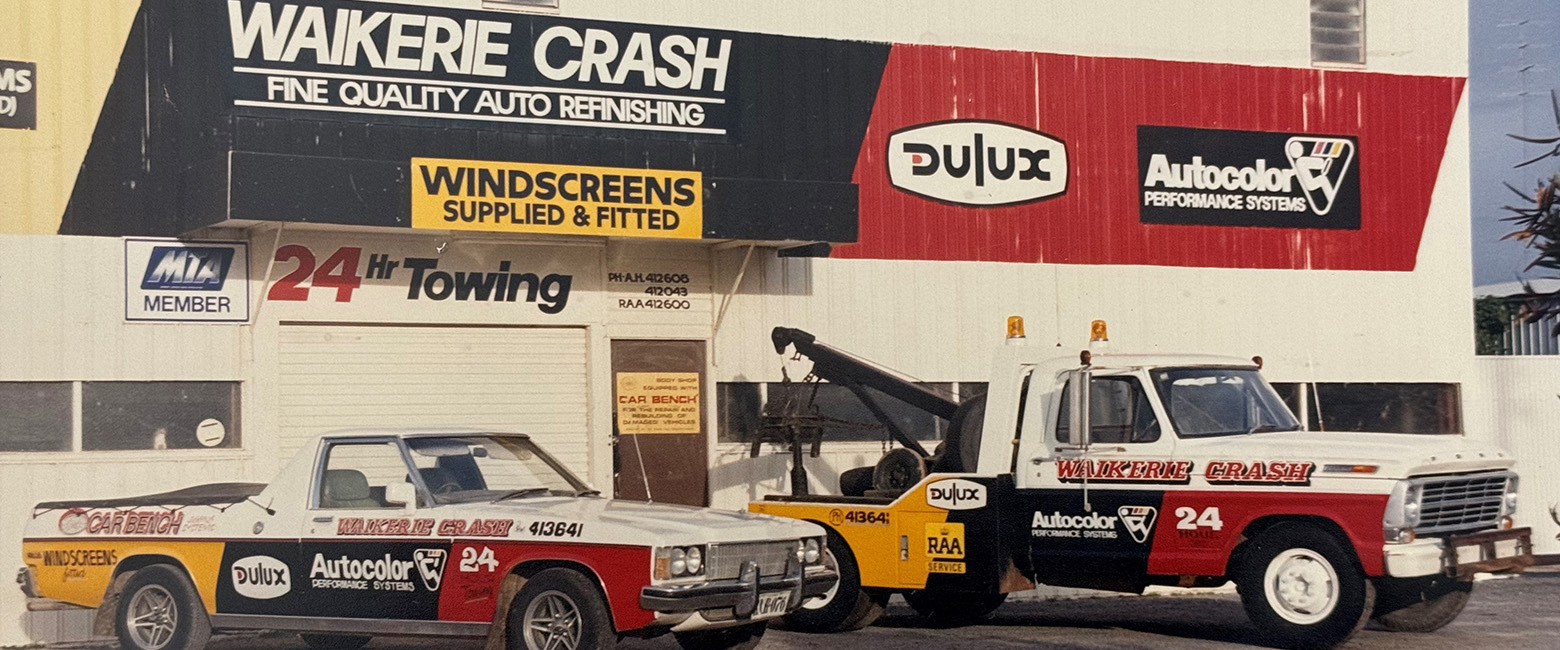 Two tow trucks parked near a building with a sign that states "Waikerie Crash," highlighting a vehicle towing service.