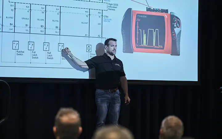An expert stands at a podium, confidently presenting to an audience at a conference, with a projector screen behind him.