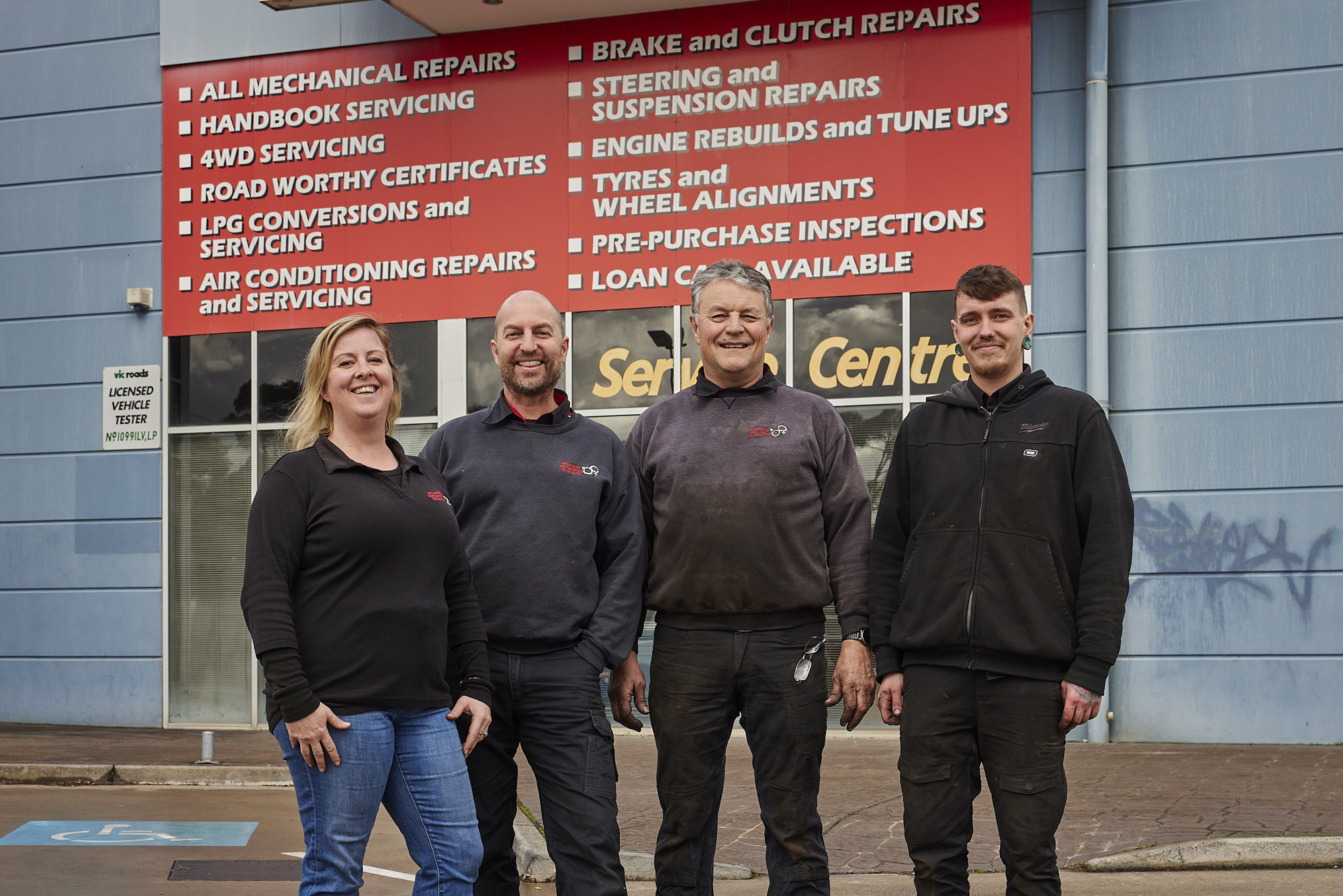 His'n'Hers Automotive Solutions Team standing in front of the workshop building and smiling to the camera