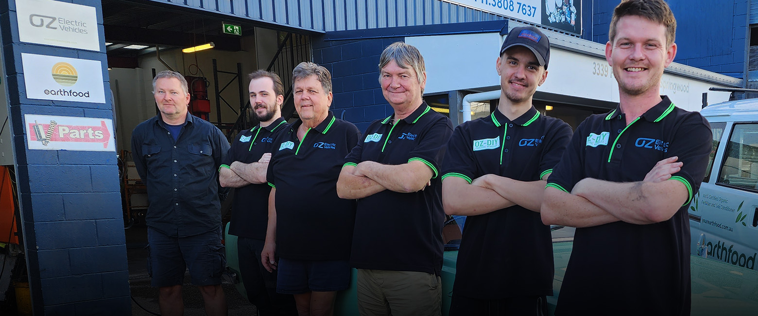 Six staff members from Oz EV standing in front of their workshop and looking to the camera smiling.
