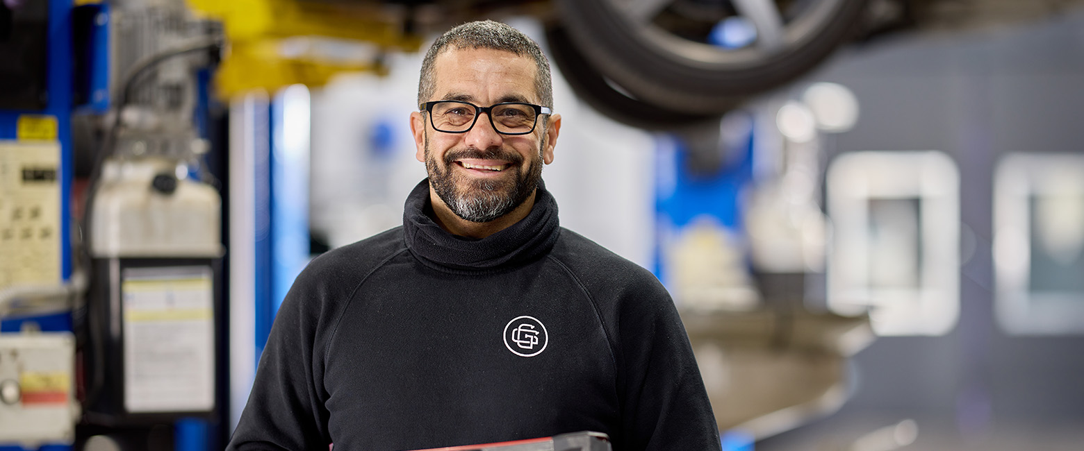 Amer Sibai, Managing Director of Glynde Garage, stands in front of a car, wearing glasses and a black shirt.